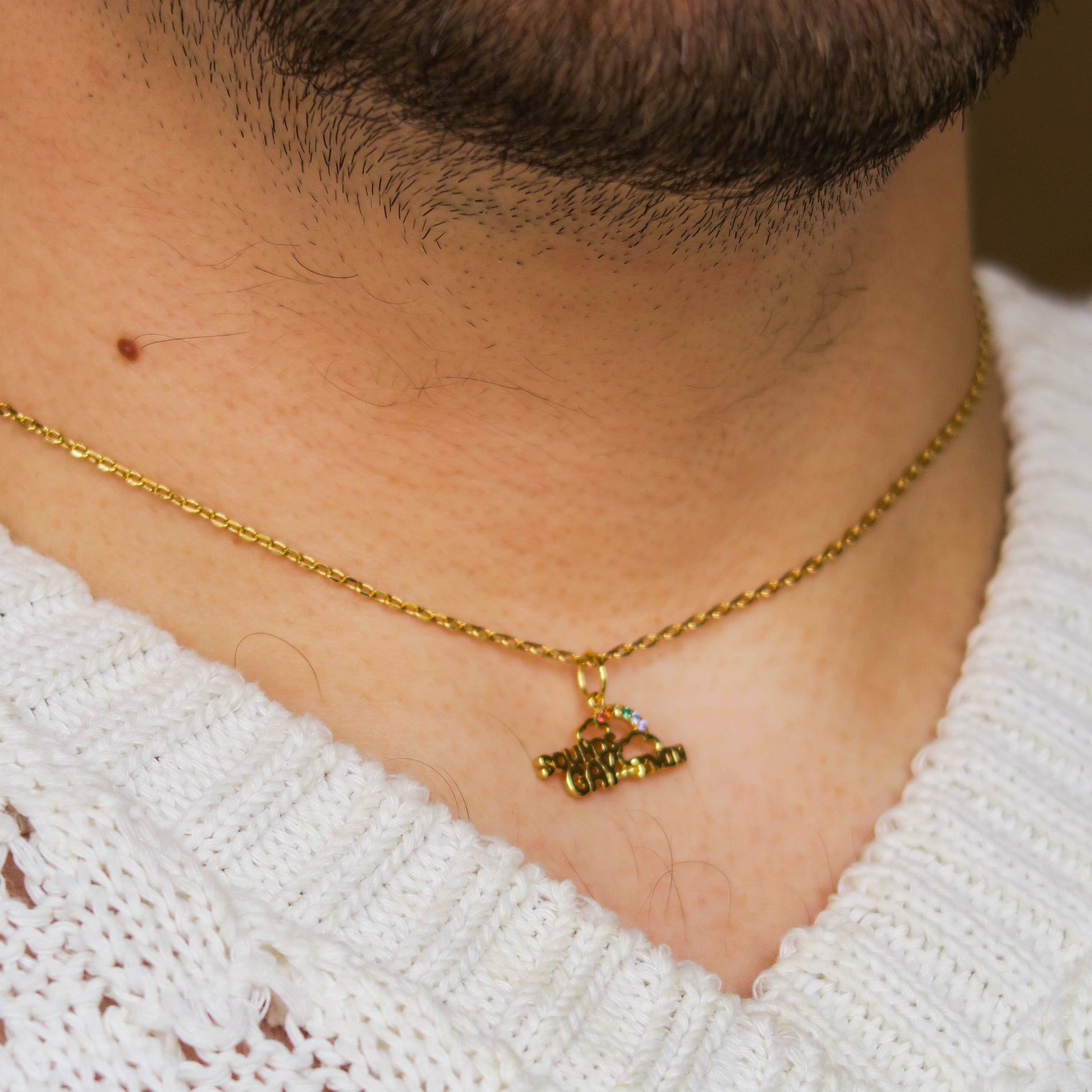 A close-up of a person wearing a gold chain with a Limited Edition PRIDE Month Charms Disco Ball Charm shaped like an airplane, paired with a white knit sweater.
