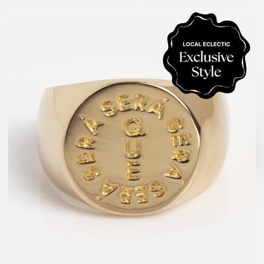 The I Like It Here Club x Local Eclectic Que Sera Sera Pinky Signet Ring features “Que Sera Sera” engraved in a circular pattern on the face with a black seal that reads “Local Eclectic Exclusive Style” in the top right corner.