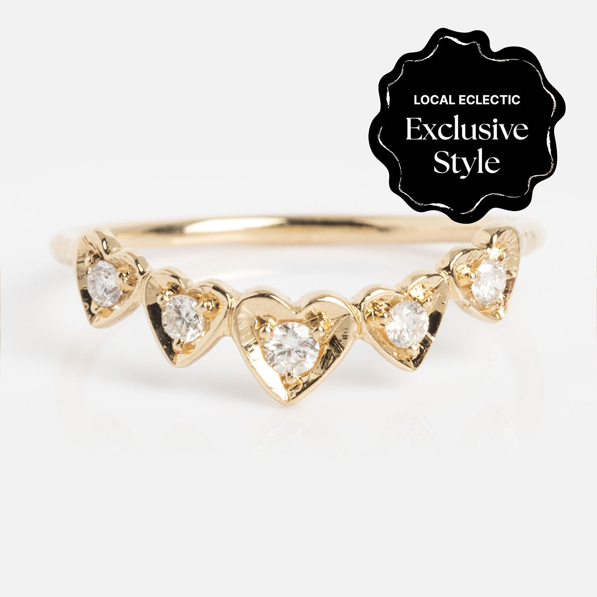 The Radiant Hearts Band (outward band) is a delicate gold ring with five heart-shaped settings, each set with a sparkling diamond (0.12 ctw), and a black "Local Eclectic Exclusive Style" label in the top right corner.