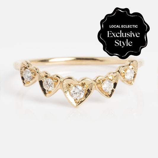 The Radiant Hearts Band (outward band) is a delicate gold ring with five heart-shaped settings, each set with a sparkling diamond (0.12 ctw), and a black "Local Eclectic Exclusive Style" label in the top right corner.