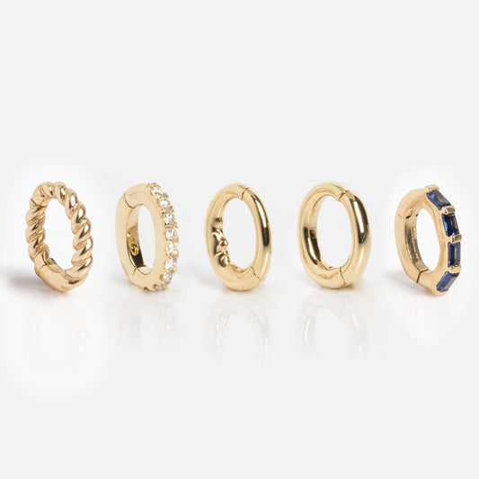 Five Solid Gold Ring Clips are displayed in a row on a white background, each with a unique design: twisted, jeweled, plain, textured, and blue-stone accented—perfect for customizing your own DIY ring stack.