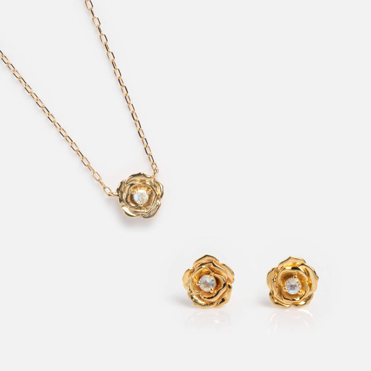 The Solid Gold Birth Flower Gift Set includes a gold necklace with a rose-shaped pendant and matching stud earrings, each featuring a clear gemstone center—an ideal jewelry gift set, beautifully displayed on a white background.