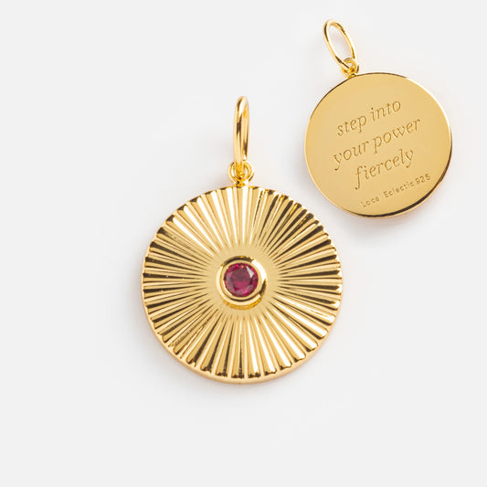 The Mantra Empowerment Coin Charm features two round 14k gold plated pendants: one with a red gemstone sunburst, the other engraved step into your power fiercely and “Luce Eclisse 925”—a striking mantra jewelry piece.