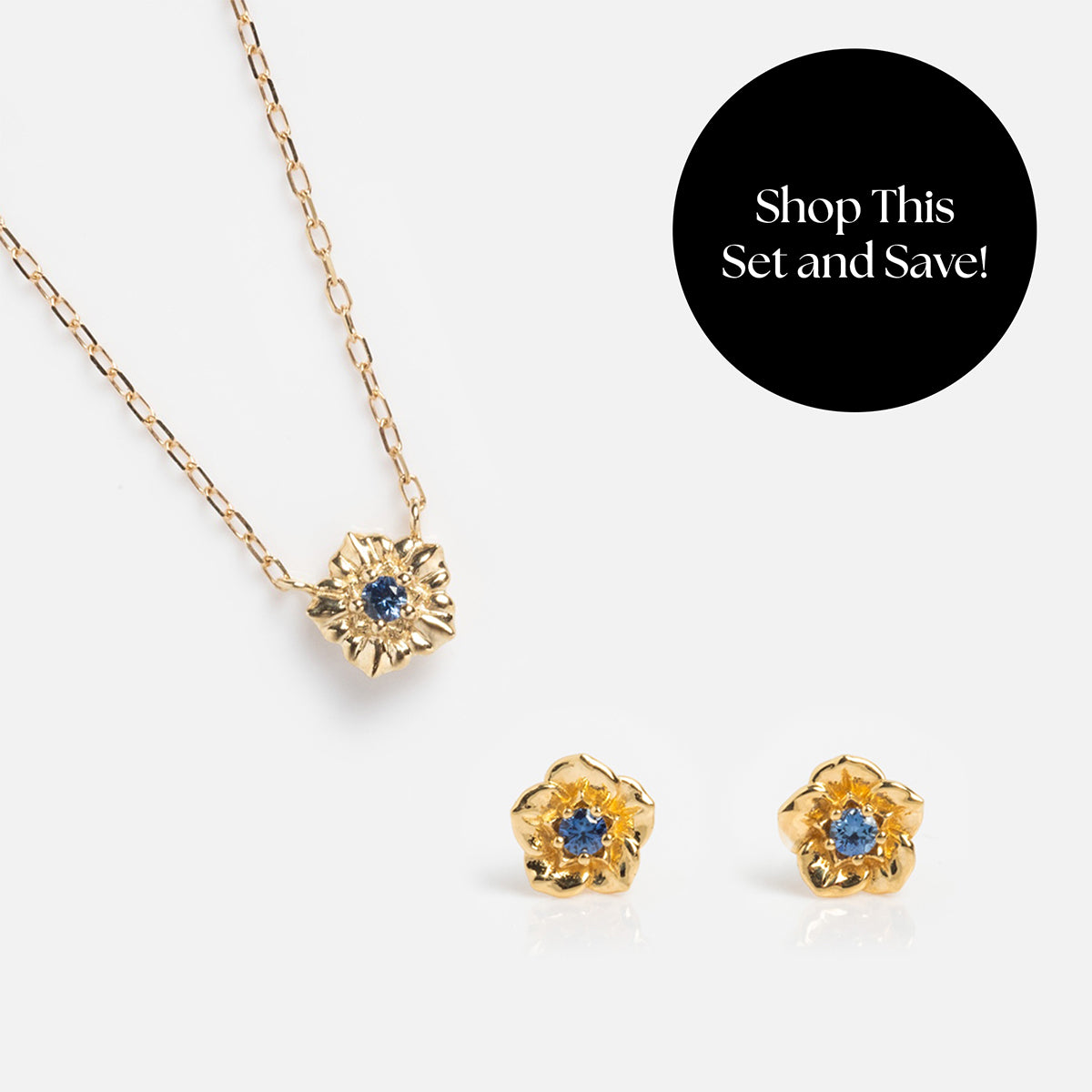 The Solid Gold Birth Flower Gift Set features a flower pendant necklace and matching earrings with blue gemstone centers, displayed on white. A black circle reads, “Shop This Set and Save!”—a perfect gold gift for someone special.