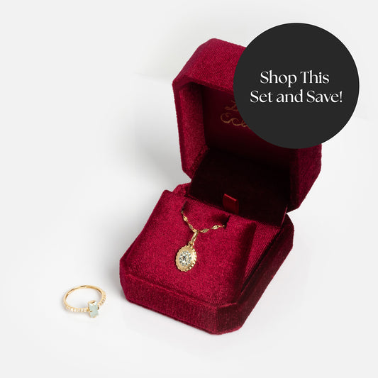 The Solid Gold 2026 March Aquamarine Capsule Set with Free Gift features a gold ring with a light blue stone and a gold pendant necklace, beautifully presented in a red velvet box. Shop this set and save!.