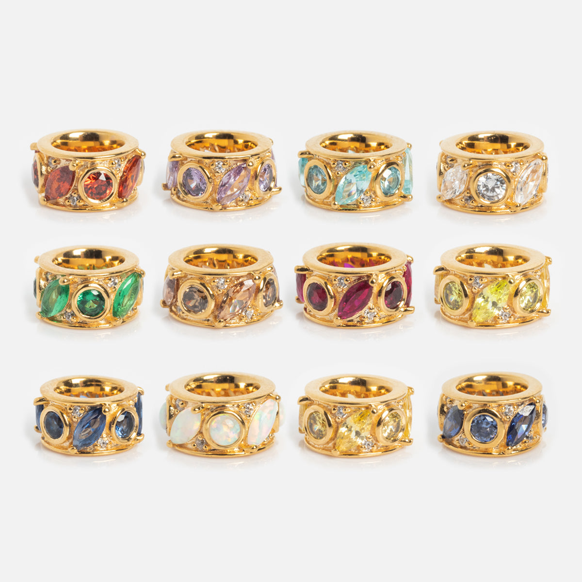Twelve Shades of You Birthstone Spacer Charms, each featuring three colorful gemstones including synthetic opal, shine in rows on a white background. These 18k yellow gold plated charms reflect Local Eclectic’s vibrant style.