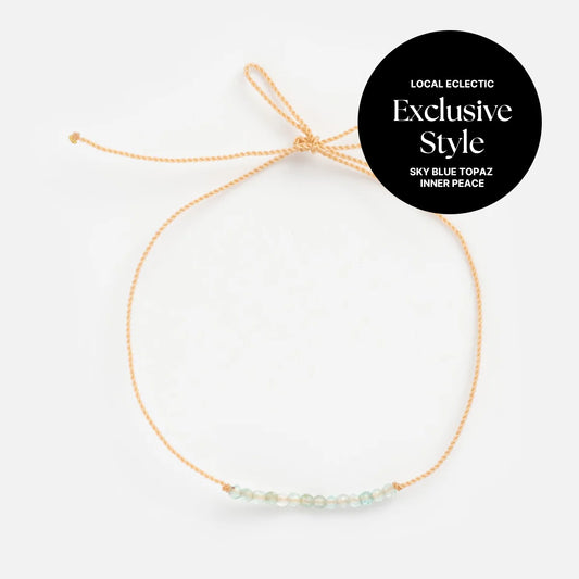Anokhi Green x Local Eclectic Gemstone Wish Bracelet with beige adjustable cord and sky blue topaz beads, labeled "Exclusive Style, Sky Blue Topaz, Inner Peace, Local Eclectic," shown on a white background.