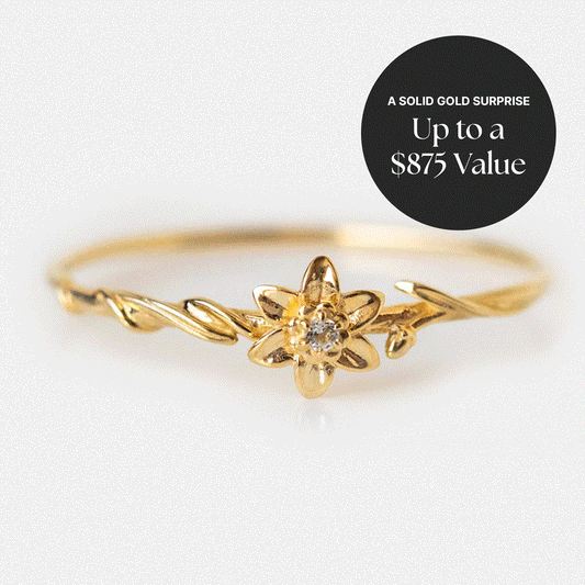 Solid Gold Surprise Ring: Delicate solid gold band with a small flower design and central gemstone, shown on a light background. Top right black circle reads, "A SOLID GOLD SURPRISE Up to a $875 Value." The perfect ring for any occasion.