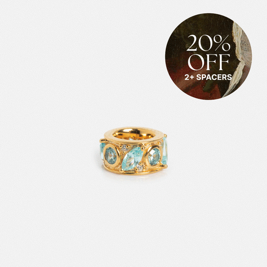 Shades of You Birthstone Spacer Charm shown on a white background with multiple blue gemstones and a gold ring. A circular overlay in the top right reads “20% OFF 2+ SPACERS” in white text. Exclusive at Local Eclectic.