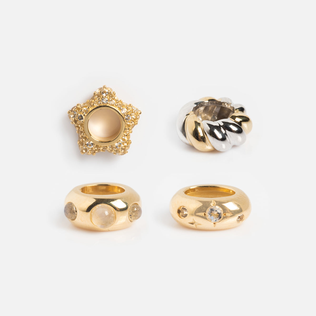 Four Solid Gold Spacer Charms are displayed on a white background, featuring a star design with crystals, a twisted silver-and-gold ring, and two gold rings adorned with sparkling stones.