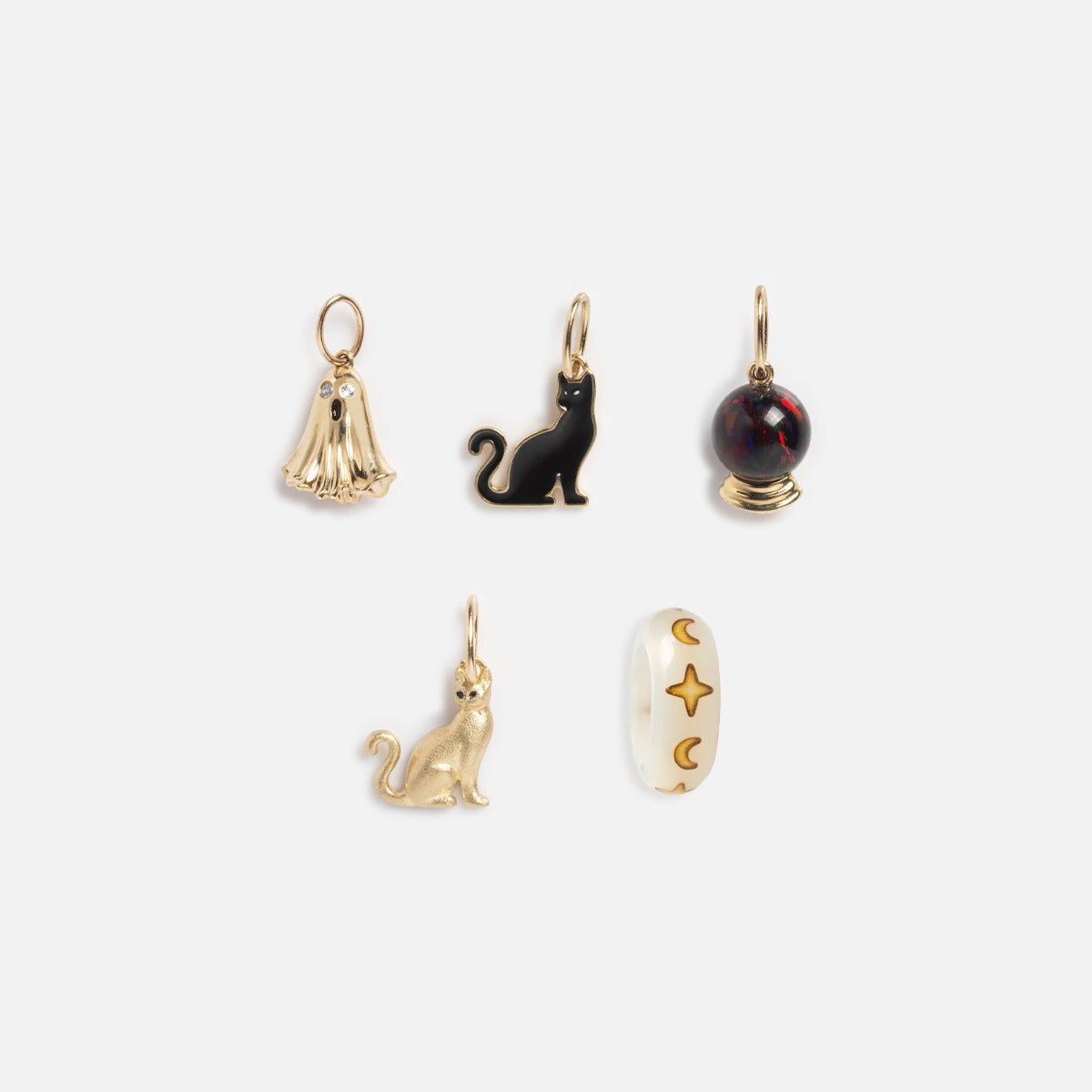 The Solid Gold Superstition Charm is featured with five small charms: a gold ghost, gold cat, black cat, deep red orb, and white oval with gold stars and crescent moons, all displayed on a plain white background.