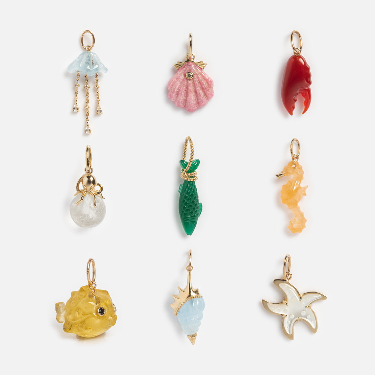 The Solid Gold Under The Sea Charm set features nine small, colorful charms shaped like sea creatures—jellyfish, seashell, seahorse, starfish, and more—each with a gold loop for hanging and a radiant inner glow.