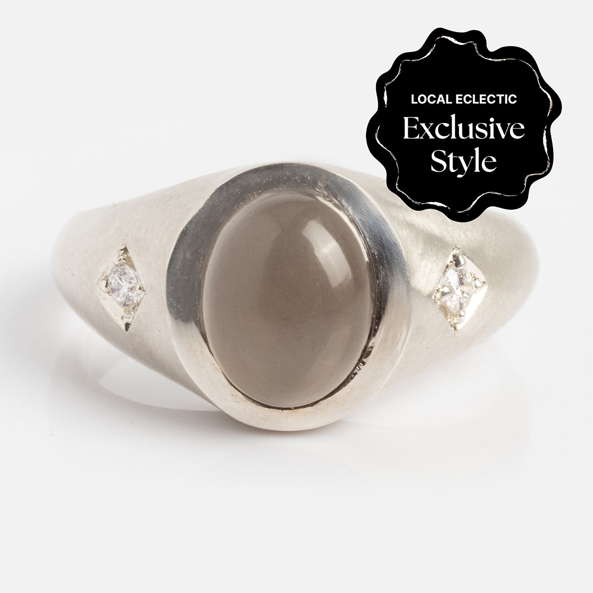 The Vailance Ring features a silver band with an oval grey moonstone center, flanked by two small diamond-shaped clear stones on each side. A black label reads "Local Eclectic Exclusive Style" in white text.