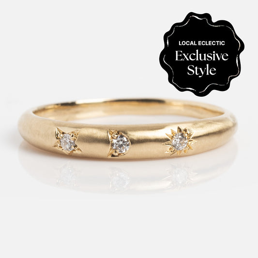 The You are my Sun, Moon and Star Band is a thin gold ring with a 1.6 mm band, featuring three small round white diamonds in distinct engraved settings. A black badge in the corner says, Local Eclectic Exclusive Style.