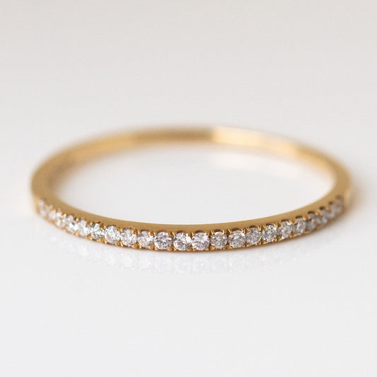 The Solid Gold Simple Pave Diamond Band in size 7 is crafted from 14k yellow gold and features small round diamonds set along the top, shown on a smooth white surface.