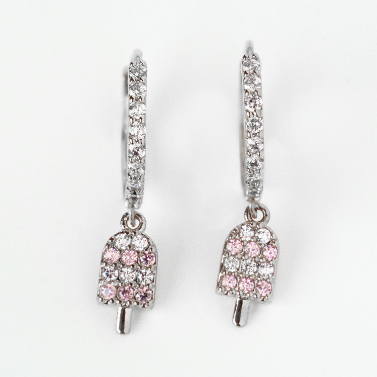 The Ice Cream Hoop Earrings Silver Sample features rhodium plated silver hoops set with clear cubic zirconia and a dangling popsicle charm adorned with pink and clear gemstones.