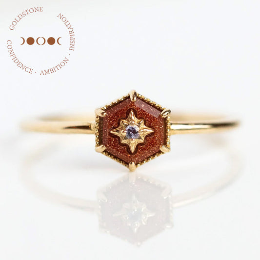 The Solid Gold Crystal Ring for Manifestation (Goldstone, Size 7) features a hexagonal goldstone centerpiece with a star-shaped iolite accent on a yellow gold band. Surrounding text: Goldstone, Confidence, Ambition, Inspiration.